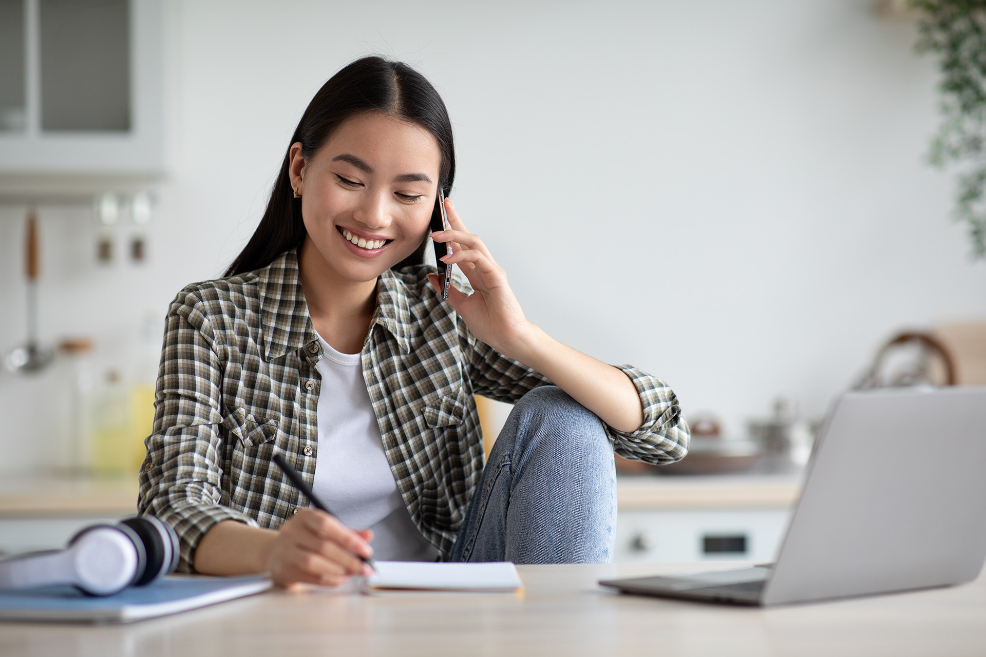 Frau telefonierend am Tisch mit Laptop